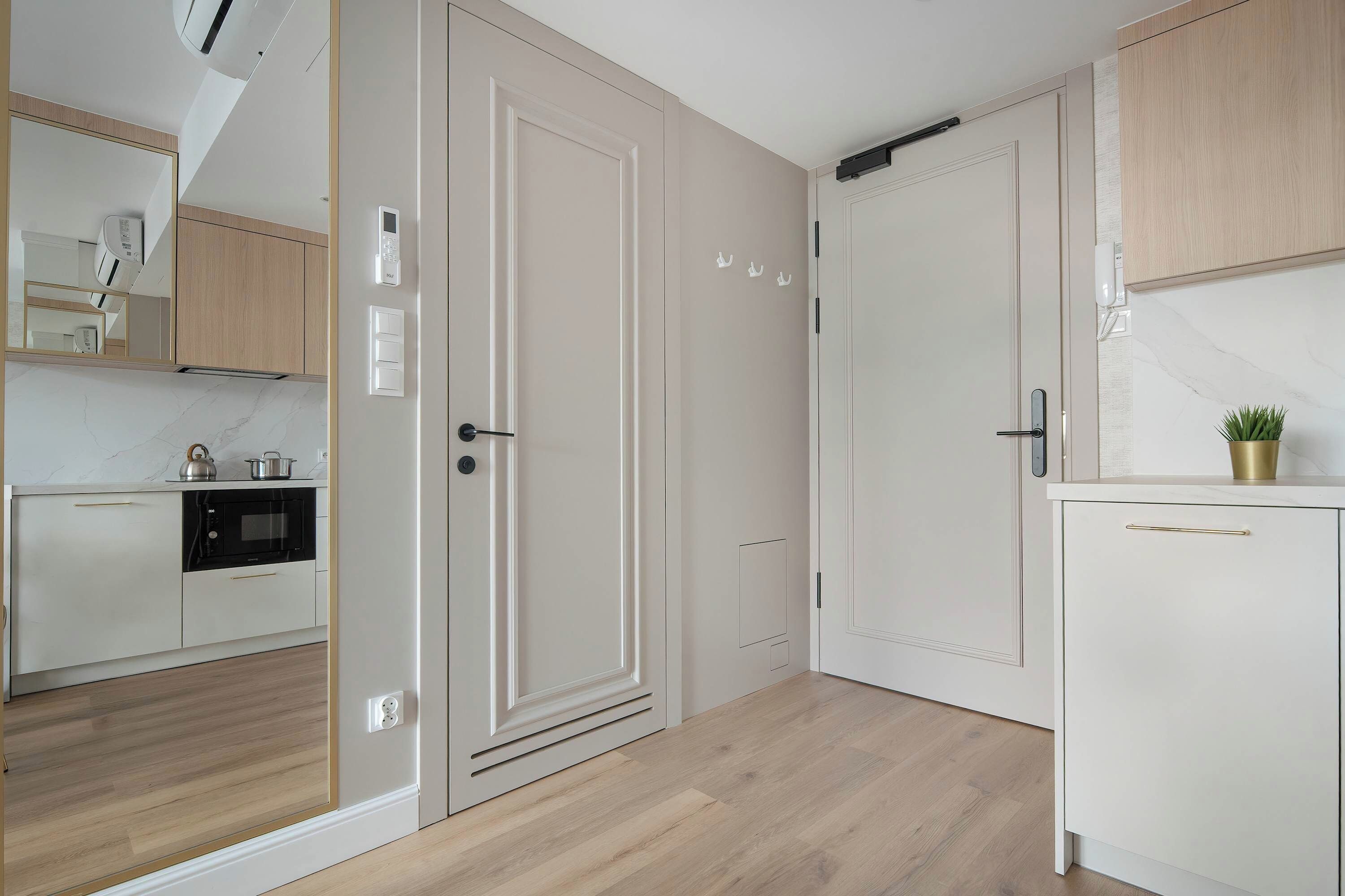 Una cocina moderna con armarios blancos, horno empotrado y microondas. Tiene piso de madera y una pequeña planta en maceta sobre la encimera.