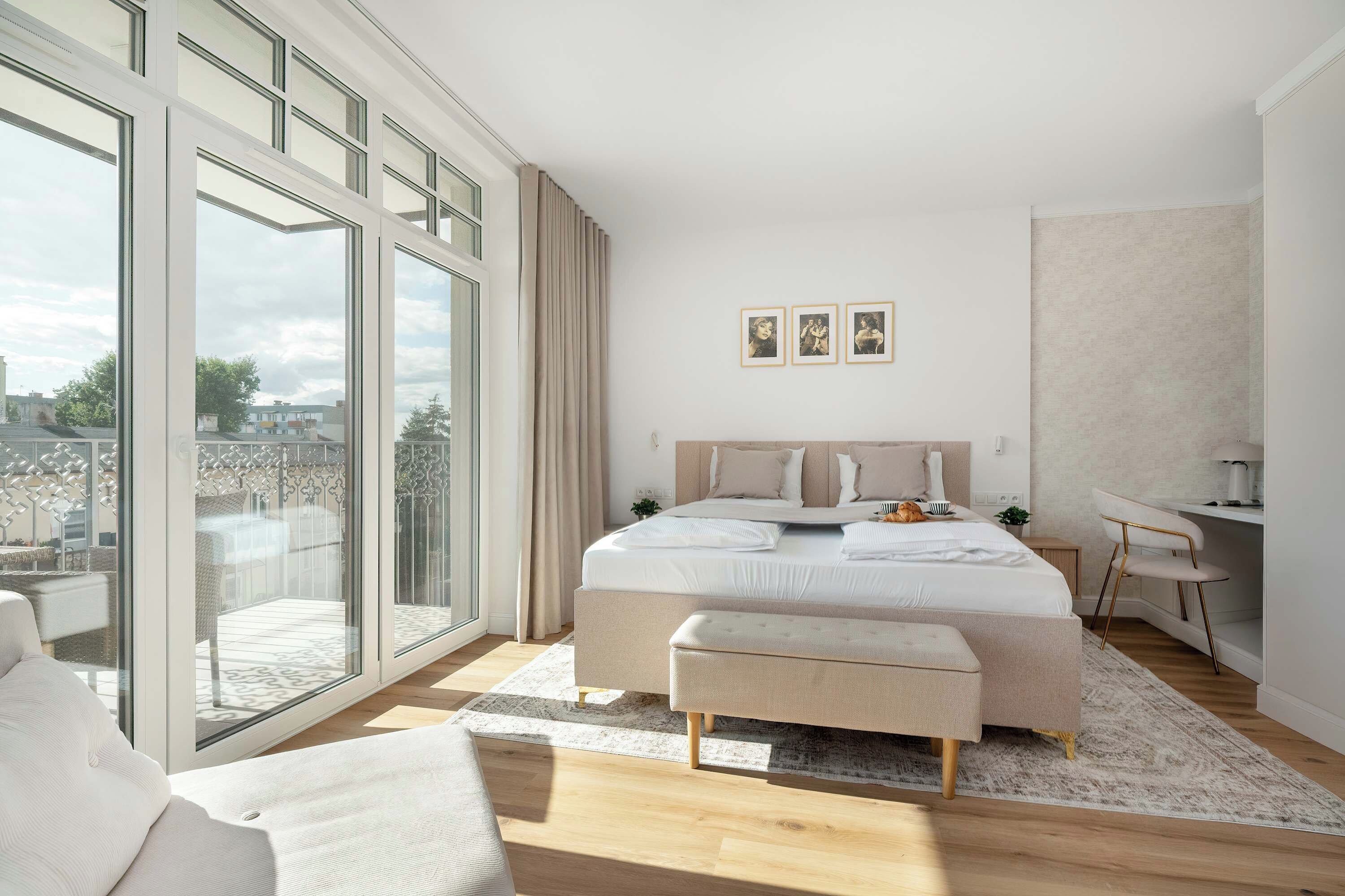 Ein modernes Schlafzimmer mit einem großen Bett, einem Schreibtisch und Blick auf die Stadt durch raumhohe Fenster.