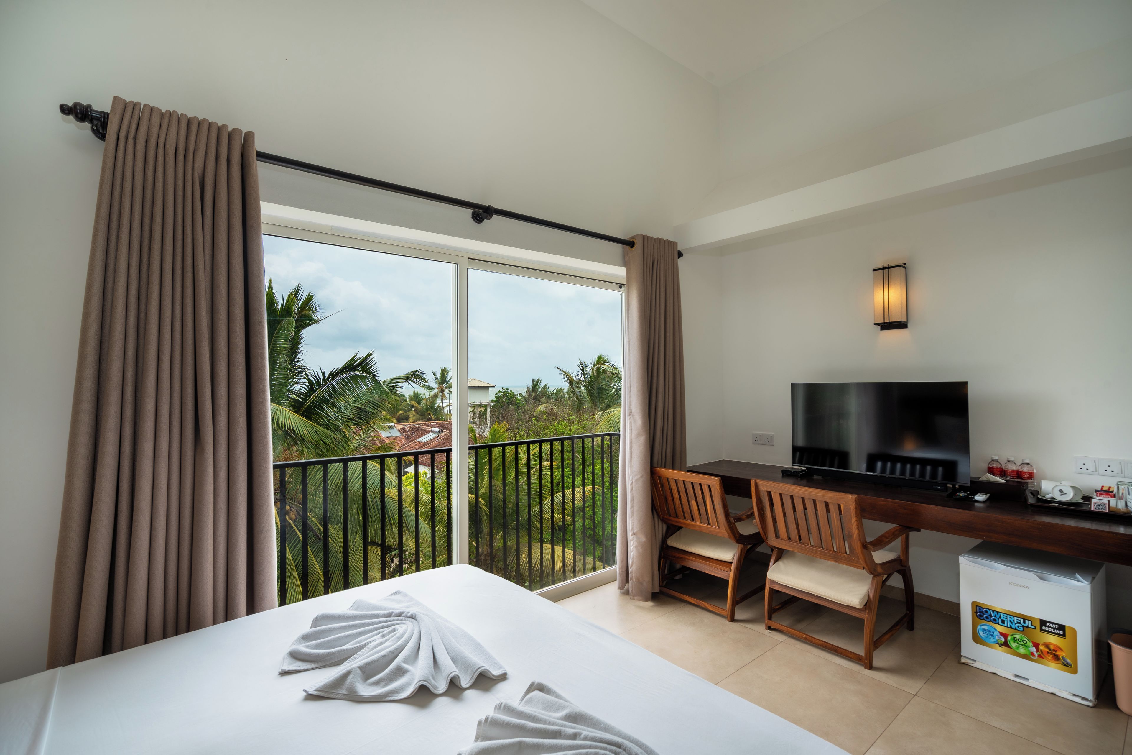 A hotel room with a bed, a desk with a TV, two chairs, and a minibar.