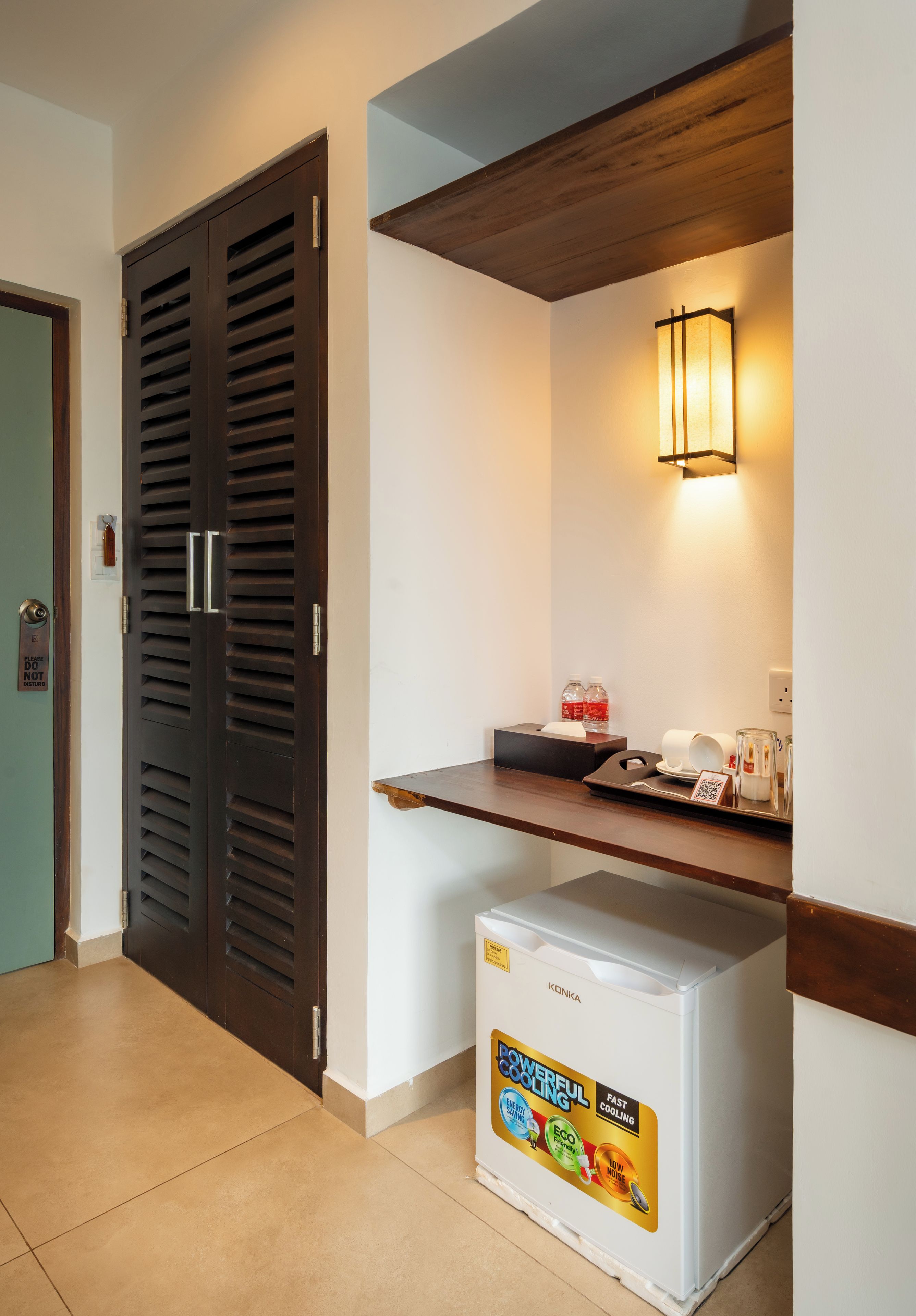 A hotel room with a minibar, a door with a 'Please do not disturb' sign, and a wall-mounted light fixture.