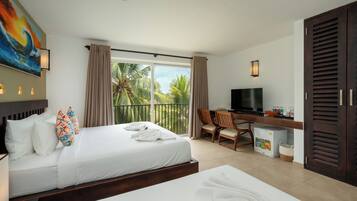 Habitación de hotel con cama, escritorio, televisor y balcón con vista a palmeras.