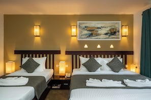 A hotel room with two beds, each with a headboard, bedside lamps, and a painting above the beds. - Rivera Tide (Bentota)