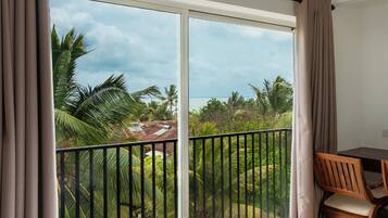 A room with a bed, a desk, and a view of a tropical landscape through a large window.