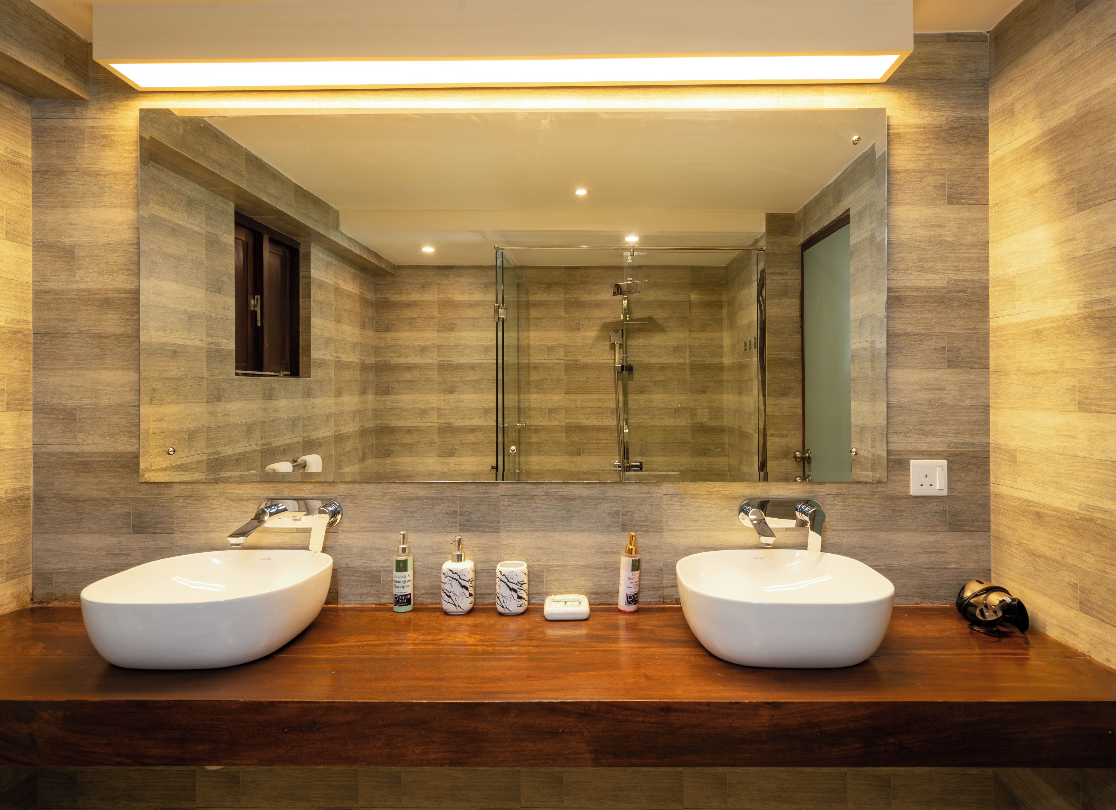 Un baño moderno con dos lavamanos, cabina de ducha de vidrio y un espejo grande.