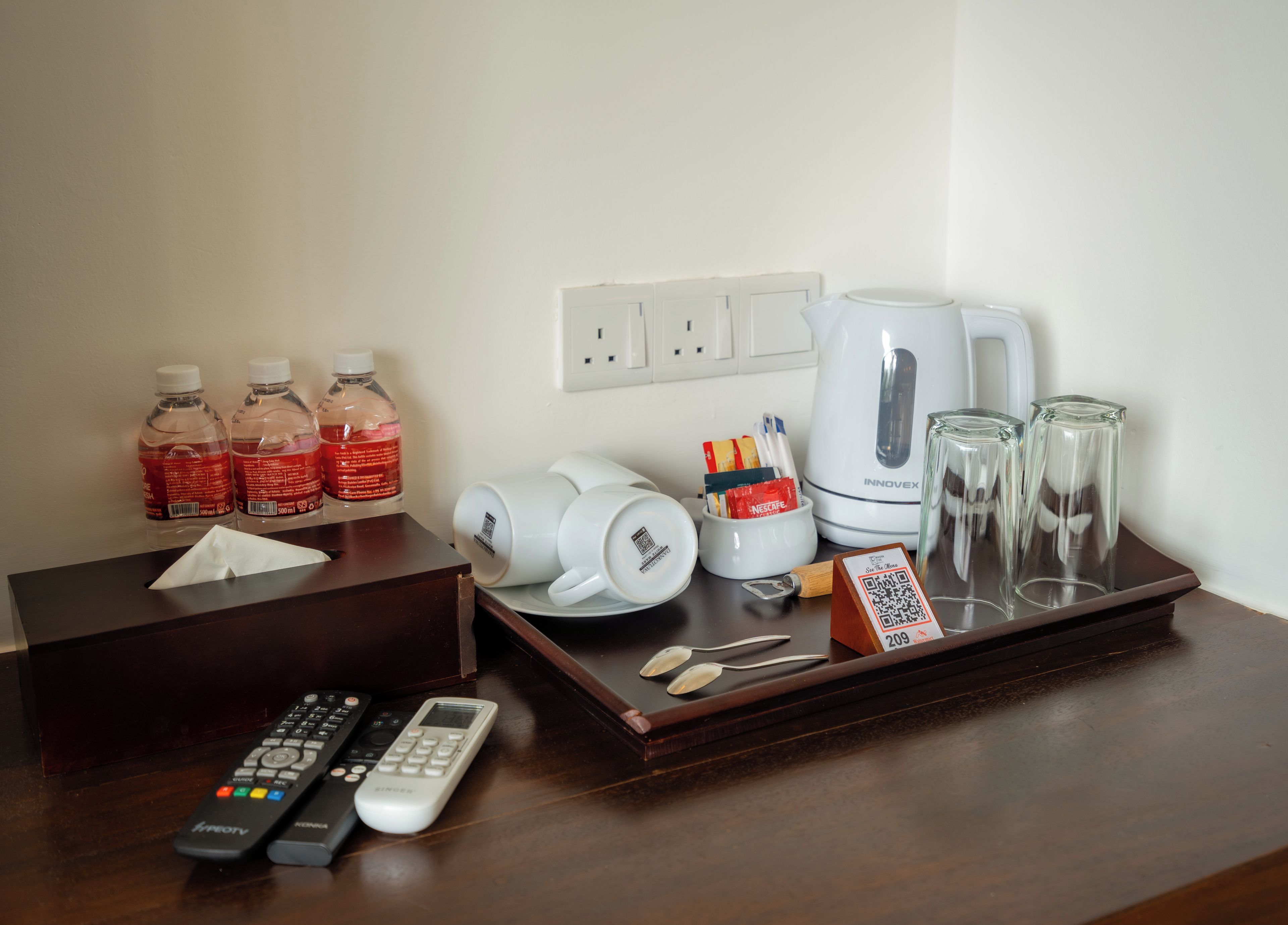 A hotel room's desk with a tissue box, remote controls, a Nespresso coffee maker, a tray with glasses, and bottled water.