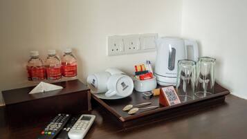 A hotel room's desk with a tissue box, remote controls, a Nespresso coffee maker, a tray with glasses, and bottled water.