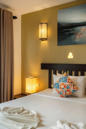 A hotel room with a bed, a nightstand, a lamp, a painting on the wall, and a window with curtains. - Rivera Tide (Bentota)