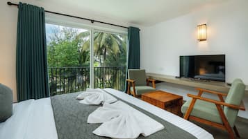 A hotel room with a bed, a TV, a chair, a small table, and a balcony with curtains.