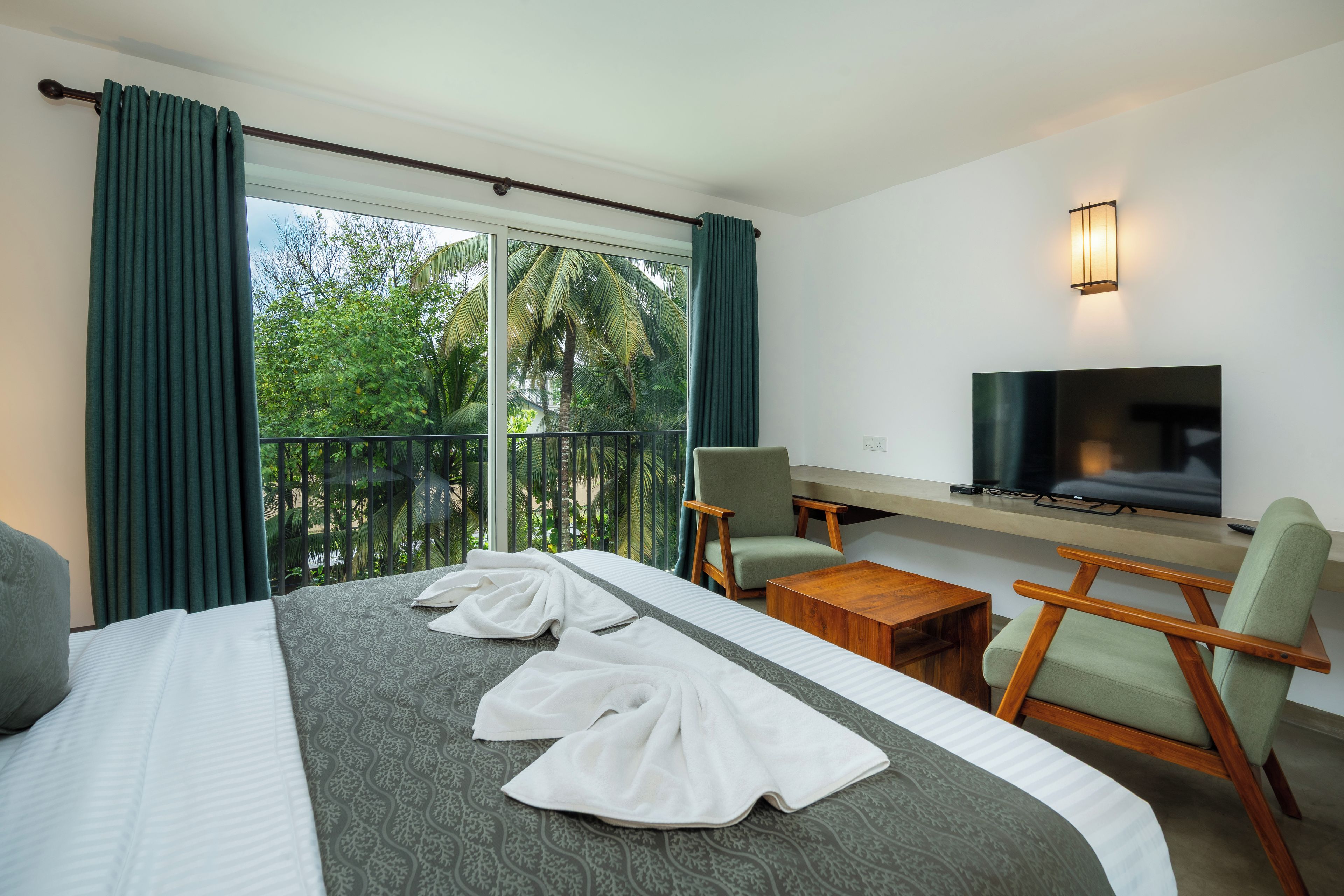 A hotel room with a bed, a TV, a chair, a small table, and a balcony with curtains.