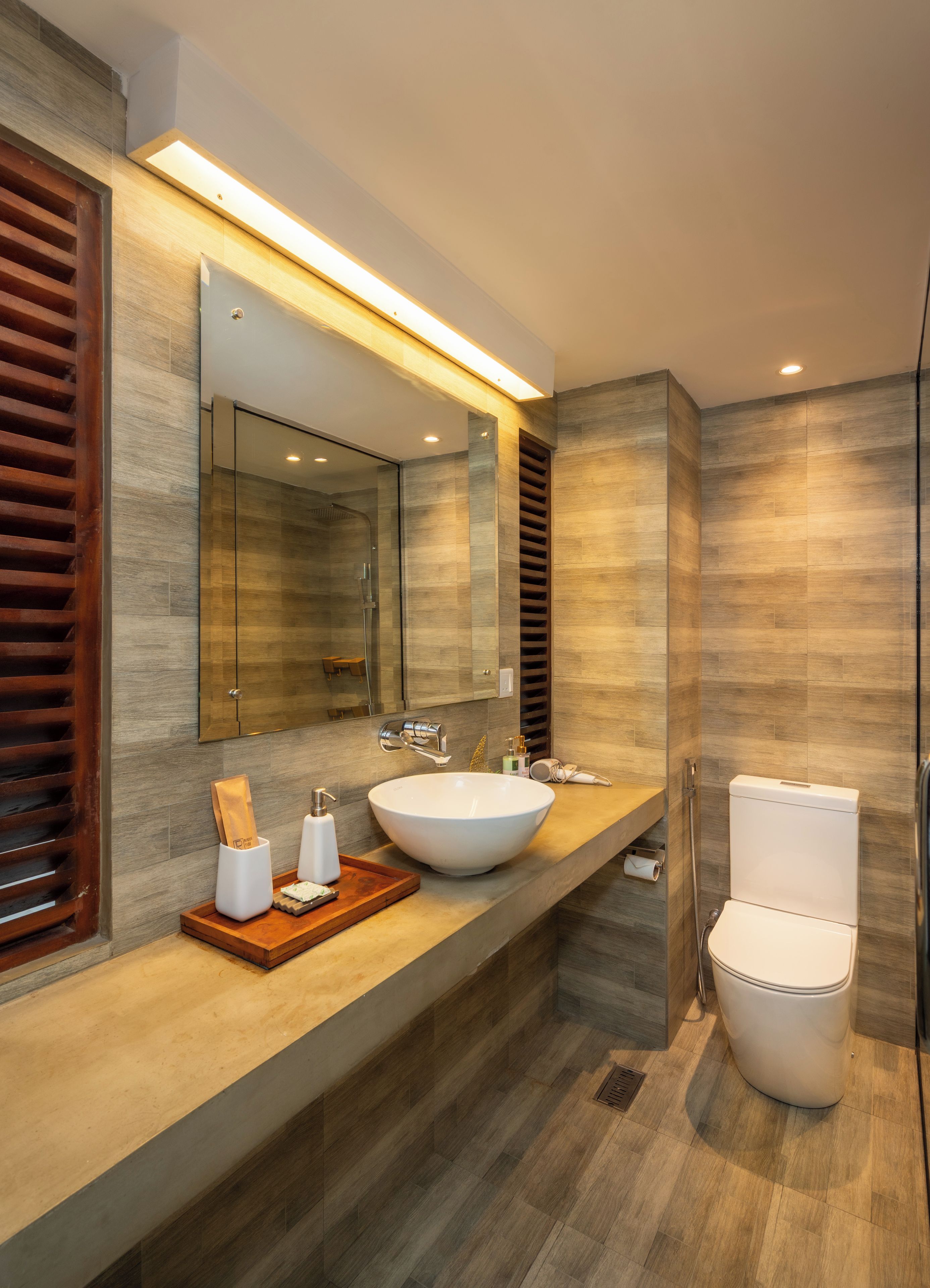A modern bathroom with a large mirror, two sinks, and a toilet.