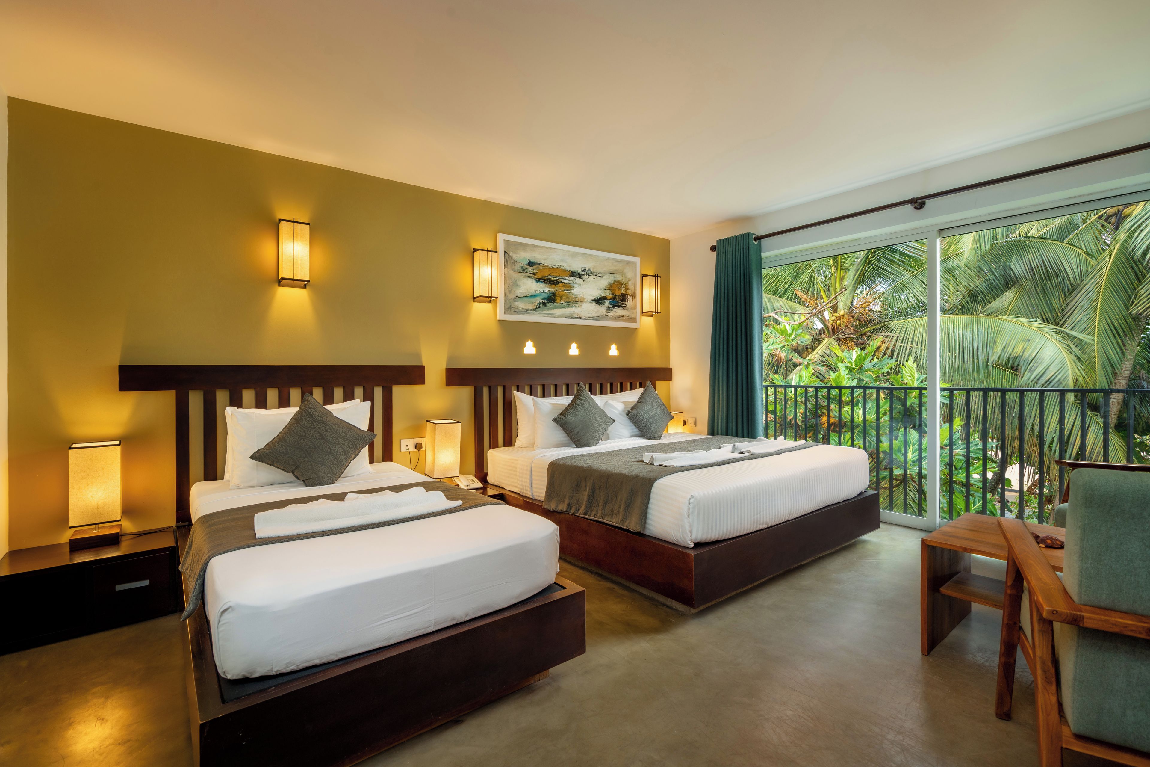 A hotel room with two beds, a painting on the wall, and a balcony with a view of palm trees.