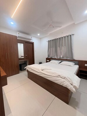 A bedroom with a bed, a wardrobe, a mirror, a ceiling fan, and a window with curtains.