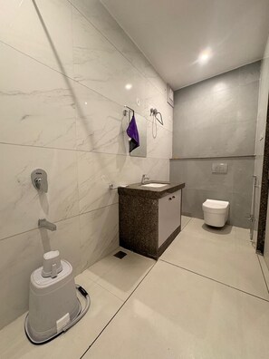 A modern bathroom with a marble floor, a sink with a dark countertop, a toilet, and a shower area.