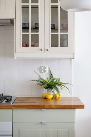A kitchen with white cabinets, a wooden countertop, a gas stove, and a potted plant with lemons. - Warsaw | Pereca 2 | Comfortable Apartment | City Centre (Warszawa)
