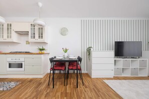 Eine moderne Küche mit weißen Schränken, einem Esstisch mit roten Kissen, einem Fernseher auf einem Schrank und einer gestreiften Wand.