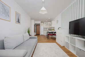 A modern living room with a grey sofa, a flat-screen TV, and a dining area with a kitchen in the background. - Warsaw | Pereca 2 | Comfortable Apartment | City Centre (Warszawa)