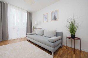 A modern living room with a grey sofa, a white rug, a potted plant, and two framed pictures on the wall. - Warsaw | Pereca 2 | Comfortable Apartment | City Centre (Warszawa)