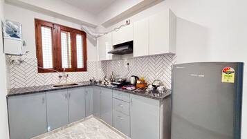 A kitchen with grey cabinets, a herringbone tile backsplash, a window with wooden frames, and a refrigerator with a sticker.