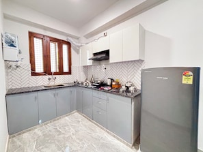 Una cocina con gabinetes grises, salpicadero de baldosas tipo espiga, una ventana con marcos de madera y un refrigerador con una etiqueta.