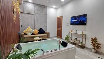 A modern living room with a large bathtub, a sofa with patterned cushions, a television, and various potted plants.