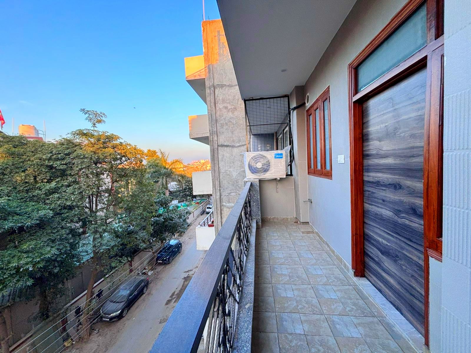 A balcony with a view of the street, a parked car, and a building with a closed shutter.