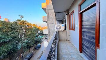 A balcony with a view of the street, a parked car, and a building with a closed shutter.