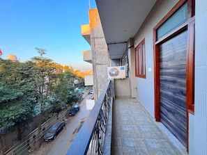 A balcony with a view of the street, a parked car, and a building with a closed shutter.