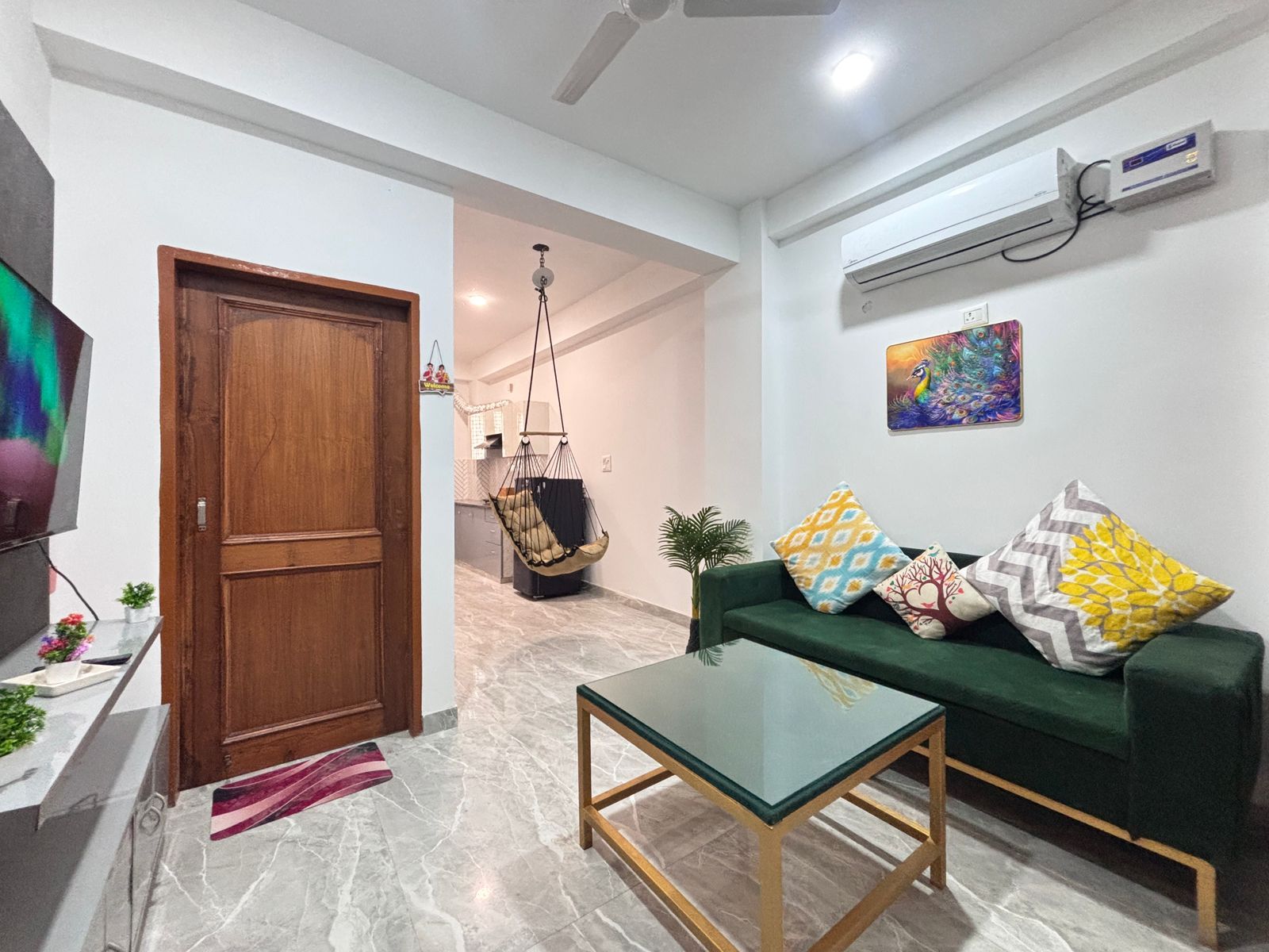 A living room with a green sofa, a glass coffee table, a wooden door, and a ceiling fan.