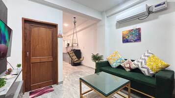 A living room with a green sofa, a glass coffee table, a wooden door, and a ceiling fan.
