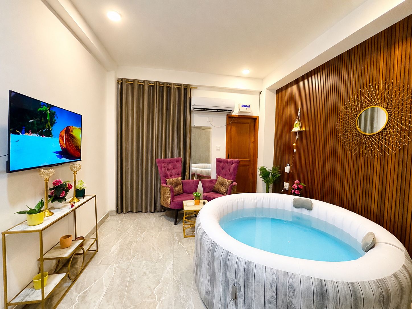 A modern living room with a large flat-screen TV, a round hot tub, and two purple armchairs.