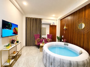 Una sala de estar moderna con un televisor de pantalla plana grande, un jacuzzi redondo y dos sillones morados.