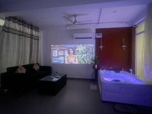 A living room with a black sofa, a coffee table, a large screen, and a bathtub with a blue light. - Instay 1BHK Service Apartment S46C (Gurugram)