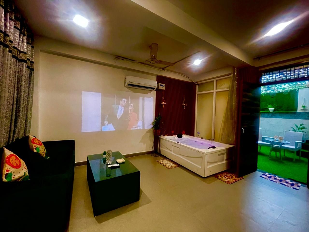 A living room with a sofa, a coffee table, a massage table, and a projection screen.