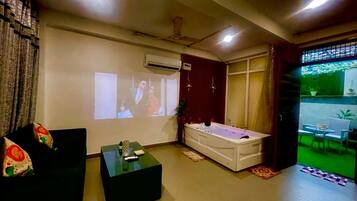 A living room with a sofa, a coffee table, a massage table, and a projection screen.