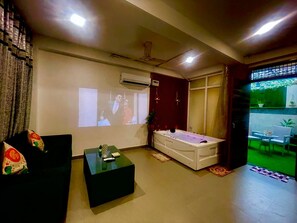 A living room with a sofa, a coffee table, a massage table, and a projection screen. - Instay 1BHK Service Apartment S46C (Gurugram)