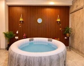 A hot tub in a room with wooden paneling, a decorative mirror, and two wall-mounted lamps.