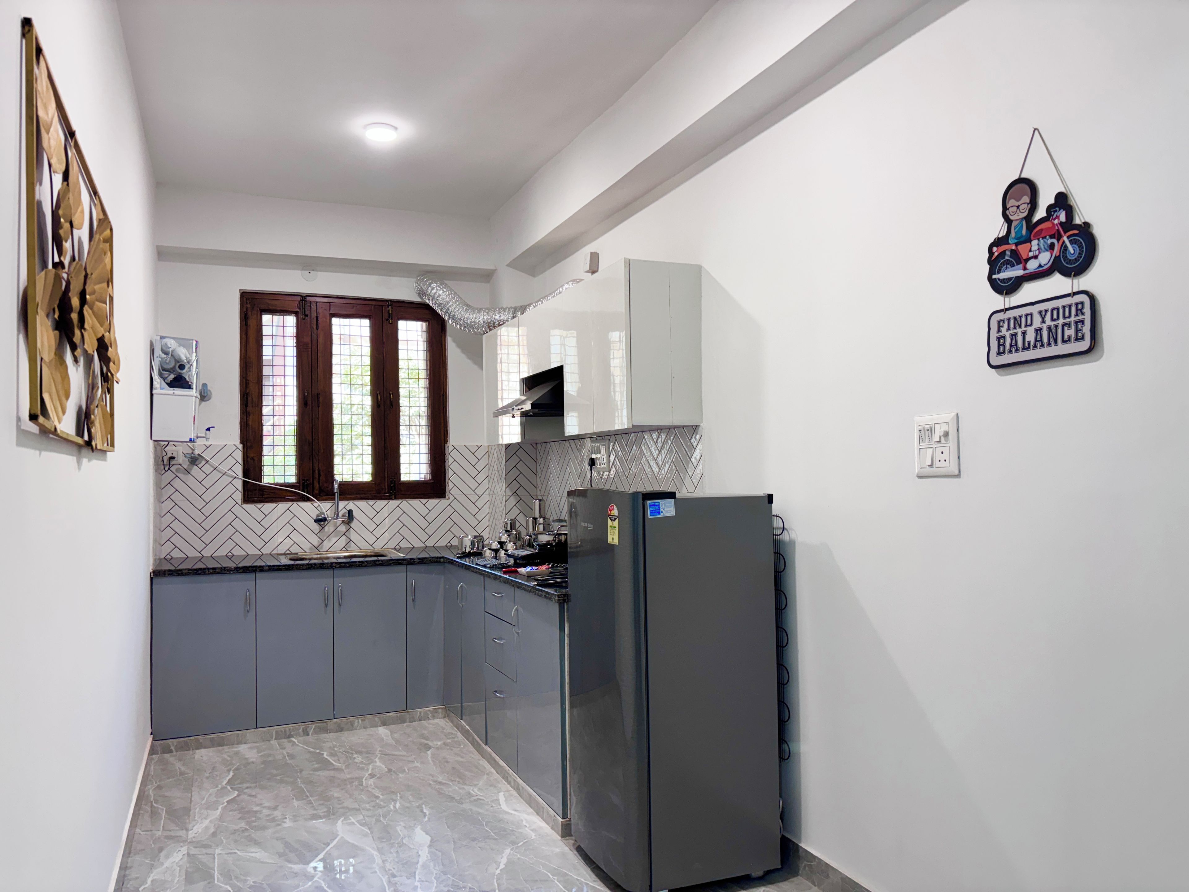 A kitchen with grey cabinets, a black refrigerator, a window with wooden frames, and a wall-mounted sign.