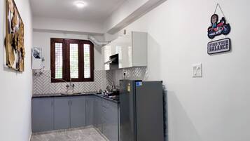 A kitchen with grey cabinets, a black refrigerator, a window with wooden frames, and a wall-mounted sign.