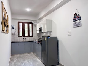 A kitchen with grey cabinets, a black refrigerator, a window with wooden frames, and a wall-mounted sign. - Instay 1BHK Service Apartment S46C (Gurugram)
