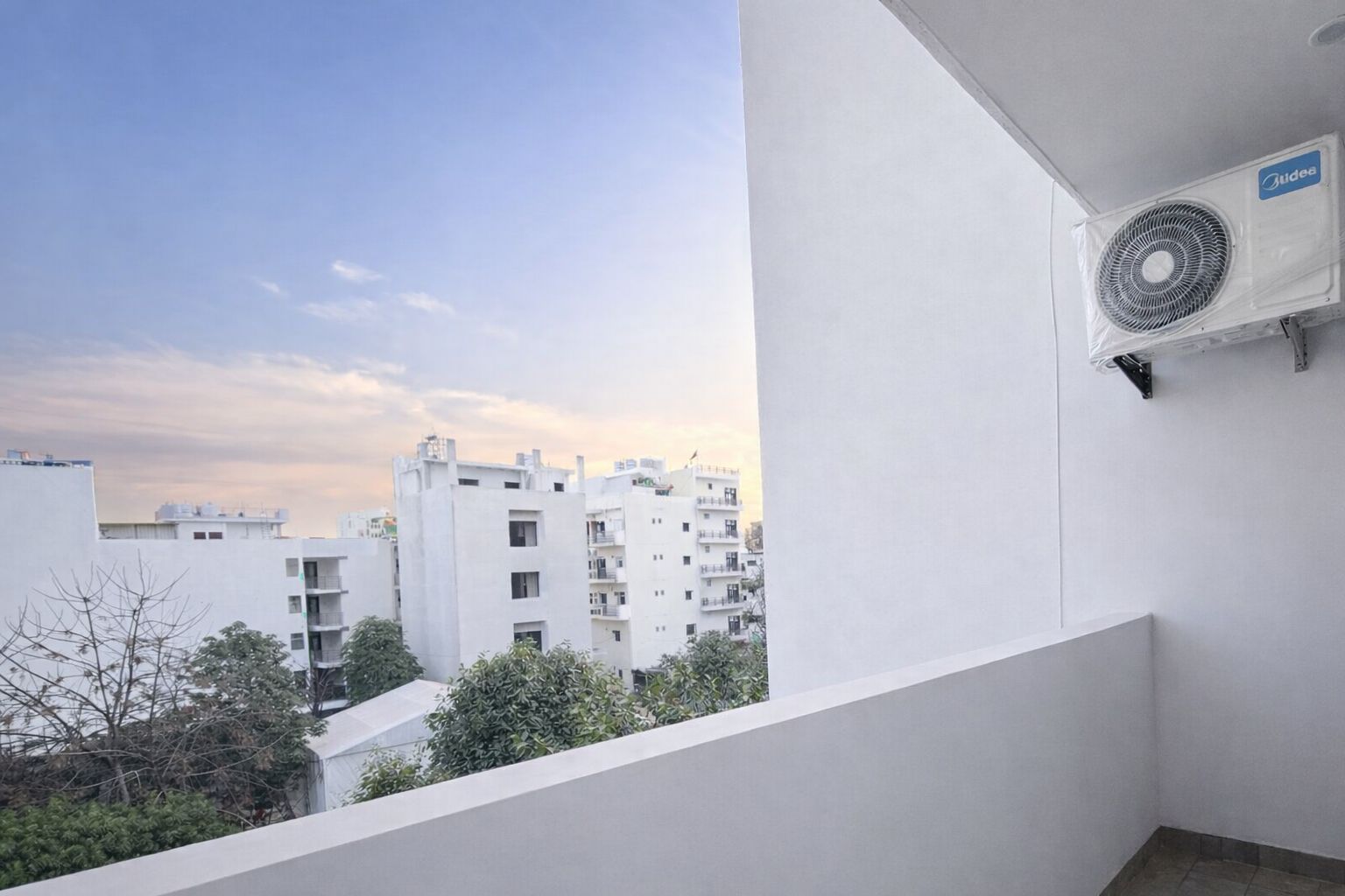 A balcony with a white wall, a ceiling fan, and a view of multi-story buildings in the background.