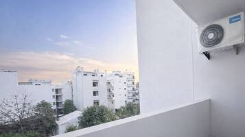 A balcony with a white wall, a ceiling fan, and a view of multi-story buildings in the background.