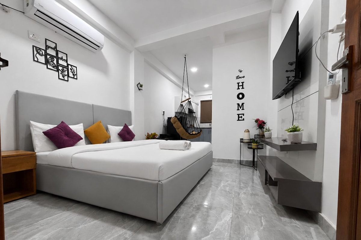 Een moderne slaapkamer met een bed, nachtkastje, hangstoel en een tv aan de muur.
