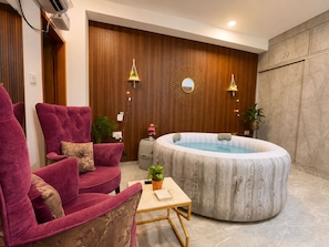 Een wellnessruimte met een bubbelbad, een rode bank en een kleine tafel met een plant.