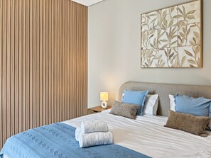 Ein Hotelzimmer mit Bett, Kissen, Nachttisch, Lampe und einem Wandbild.