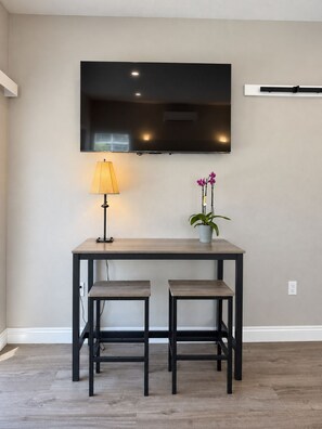 A modern room with a flat-screen TV mounted on the wall, a small table with a lamp and a potted plant, and two matching chairs. - Serene Brand New studio with AC in charming La Palma  (La Palma)