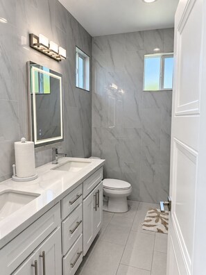 A modern bathroom with marble walls, a large mirror, a toilet, and a vanity with a sink and drawers. - Serene Brand New studio with AC in charming La Palma  (La Palma)