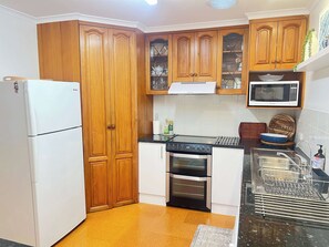 Eine kleine Küche mit Holdekor-Schränken, einem weißen Kühlschrank, einer Mikrowelle, einem Backofen und einem Spülbecken mit Geschirrgestell.
