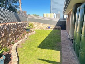 Ein Garten mit einer Mauer aus Stein, einer Rasenfläche und einem Pflasterweg, der zu einem Gebäude führt.