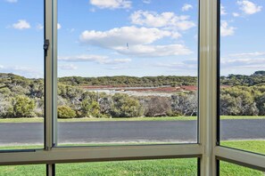 Blick durch ein Fenster auf eine Straße, die zu einer hügeligen Landschaft mit dichter Vegetation und blauem Himmel führt.