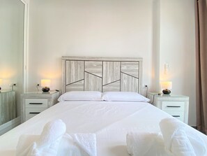 A hotel room with a large bed, two bedside tables with lamps, and a wooden headboard. - Apartment in Nerja With Sea Views & Pool (Nerja)